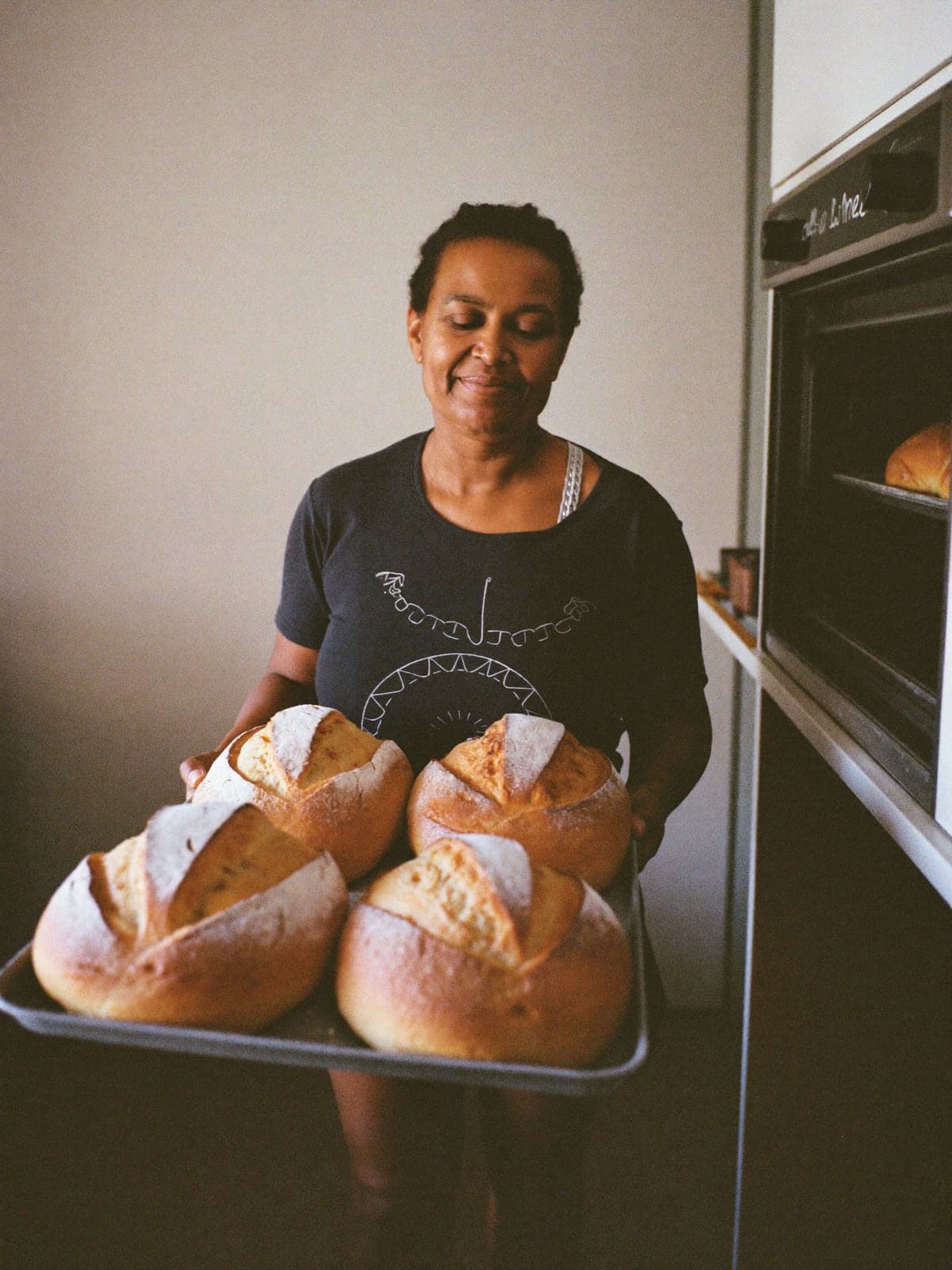 Padeira segurando uma bandeja de pães caseiros recém saídos do forno.