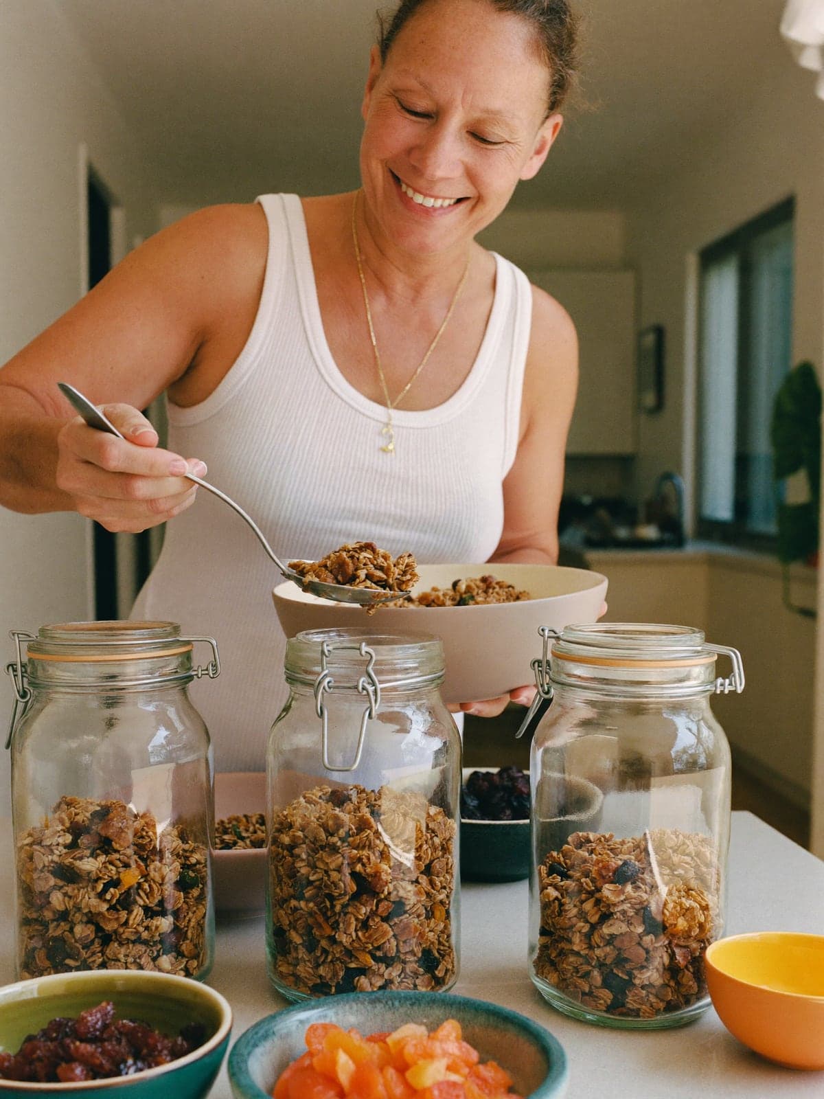 Mulher colocando granola caseira em potes de vidro com tampa, na mesa da cozinha.